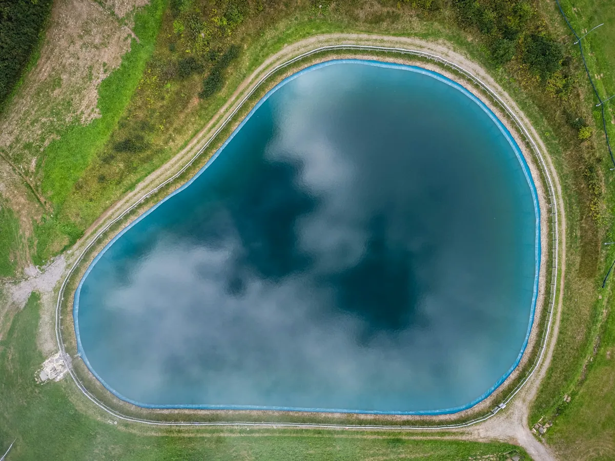 Aerial view of a lined water reservoir surrounded by grass and an access track.
