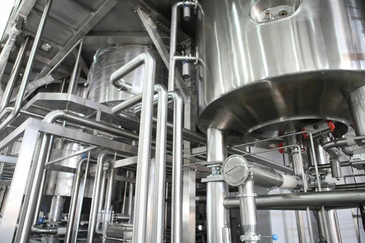 Stainless-steel process vessels, pipes and an access stair inside an industrial facility.
