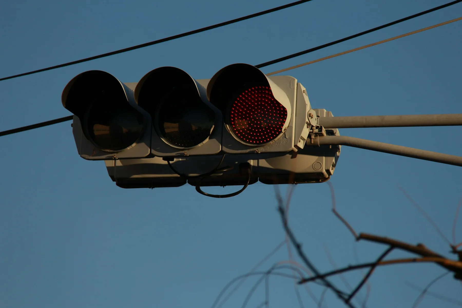 Weathered horizontal traffic-signal head suspended beside overhead cables.