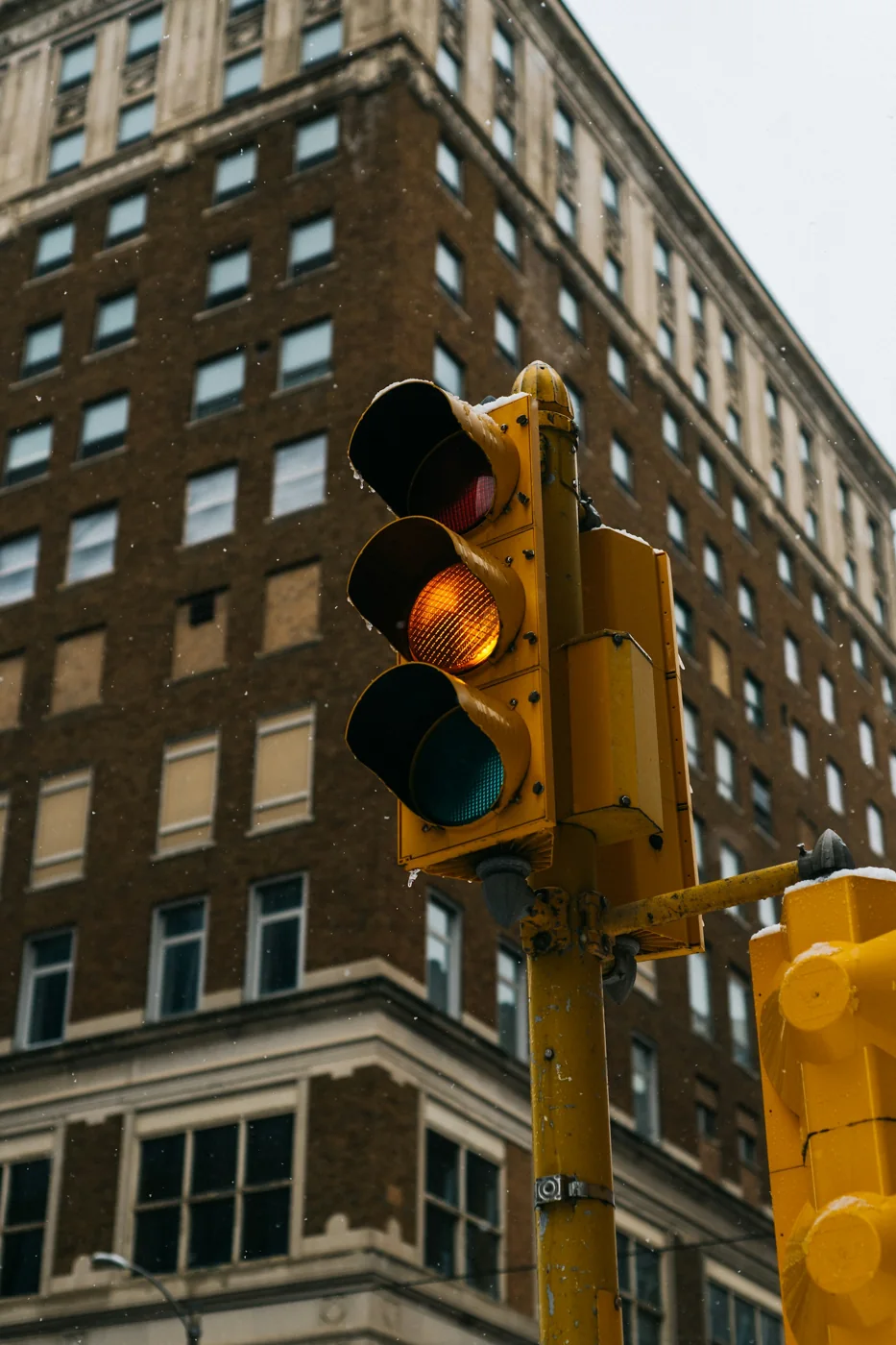 Yellow traffic-signal housing beside a city building with the amber lamp illuminated.