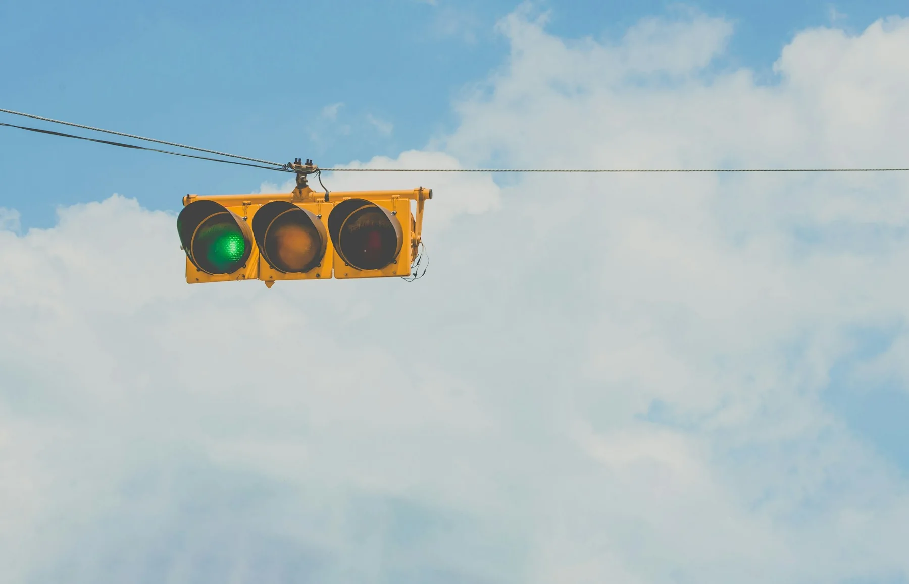 Horizontal traffic-signal head with its green lamp illuminated against a bright blue sky.