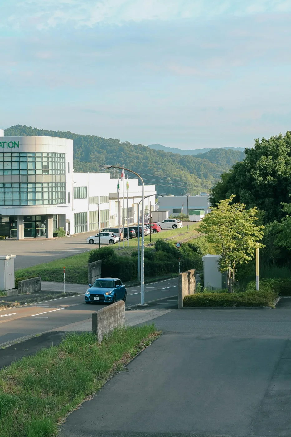 Blue car on an access road beside a modern office building and trees.