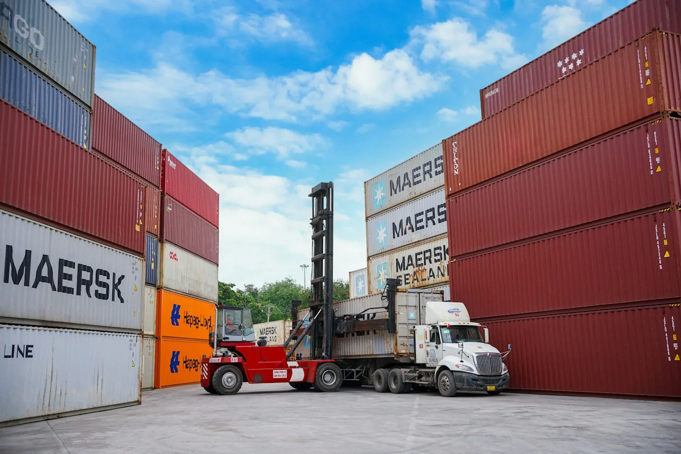 Container handler and truck between rows of stacked shipping containers.