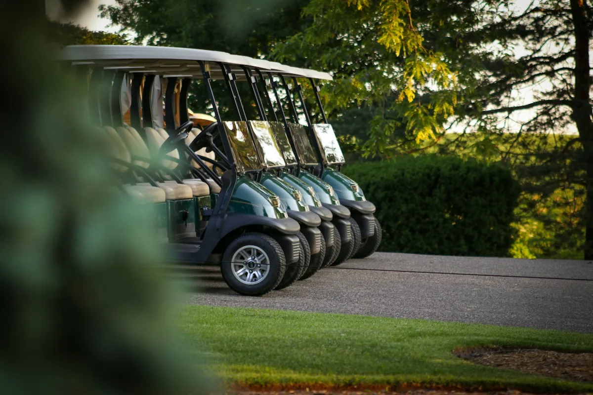 A row of golf carts parked beside trees at a golf facility.