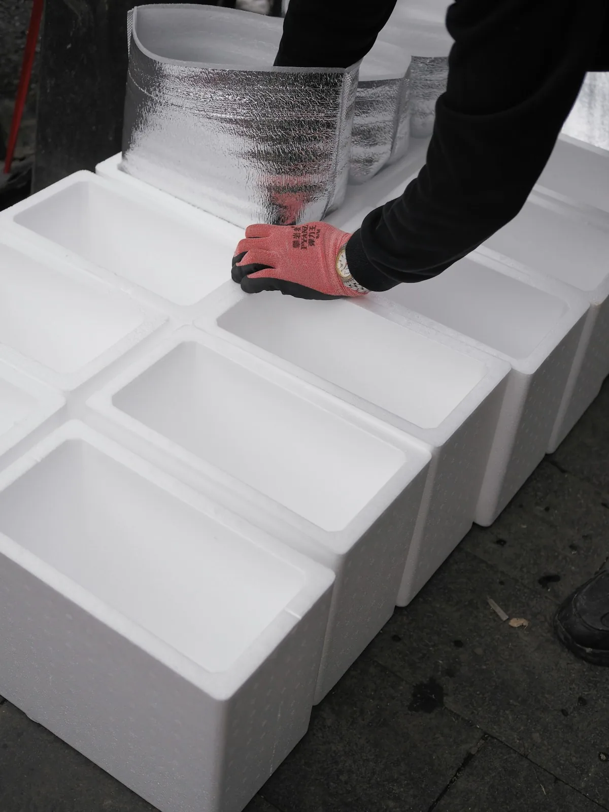 A worker packing white insulated boxes with clear wrapping.