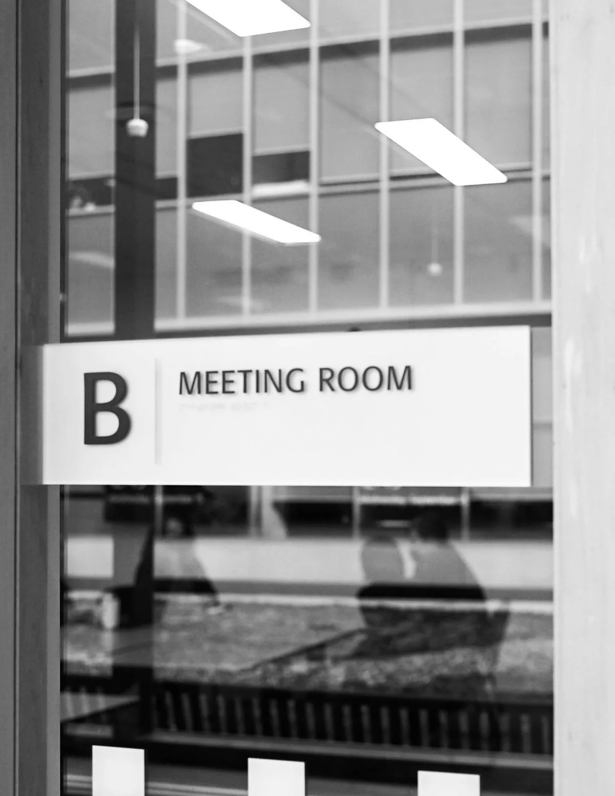 A printed meeting-room label on a glass office door.