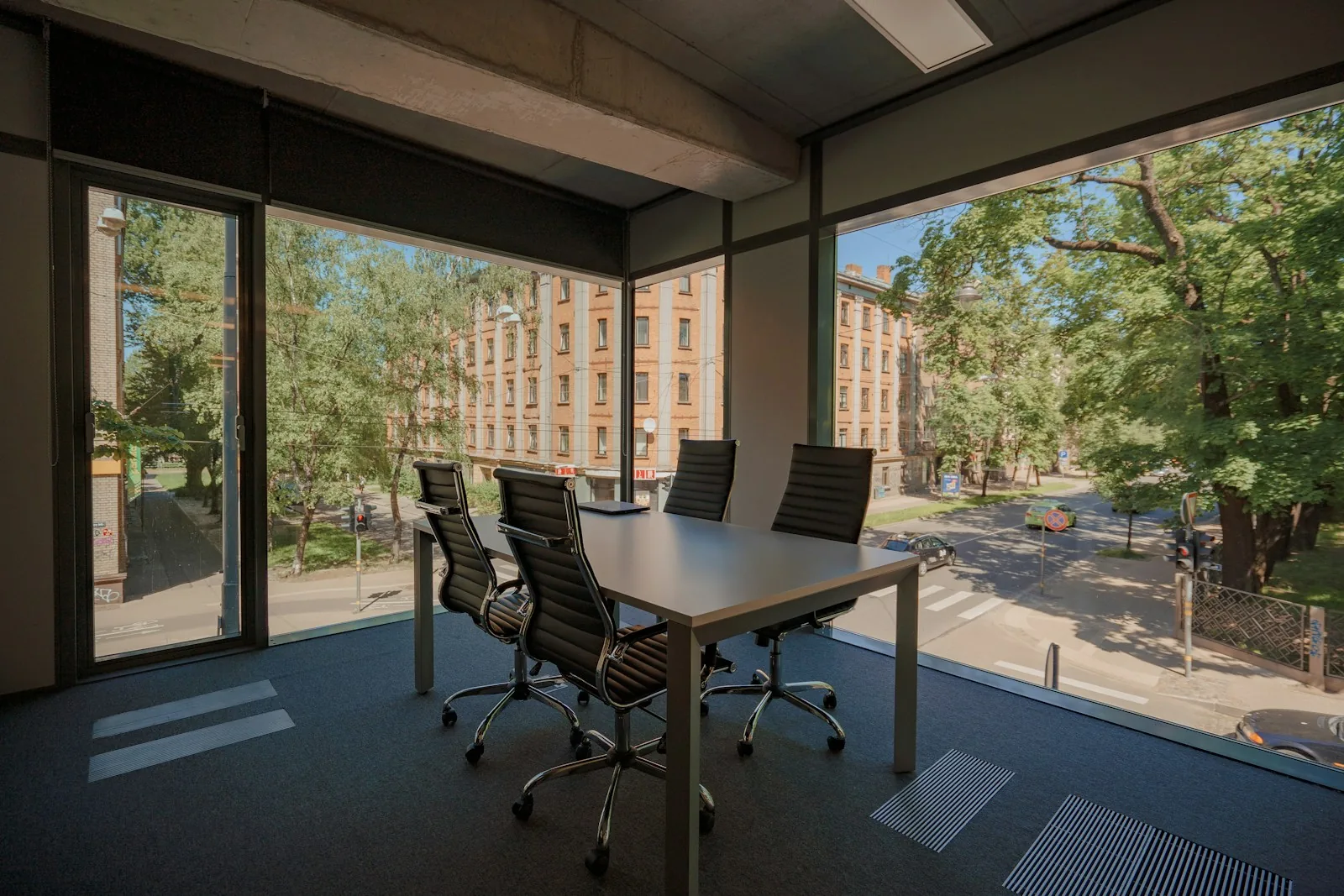 Empty corner meeting room with floor-to-ceiling windows and floor ventilation grilles.