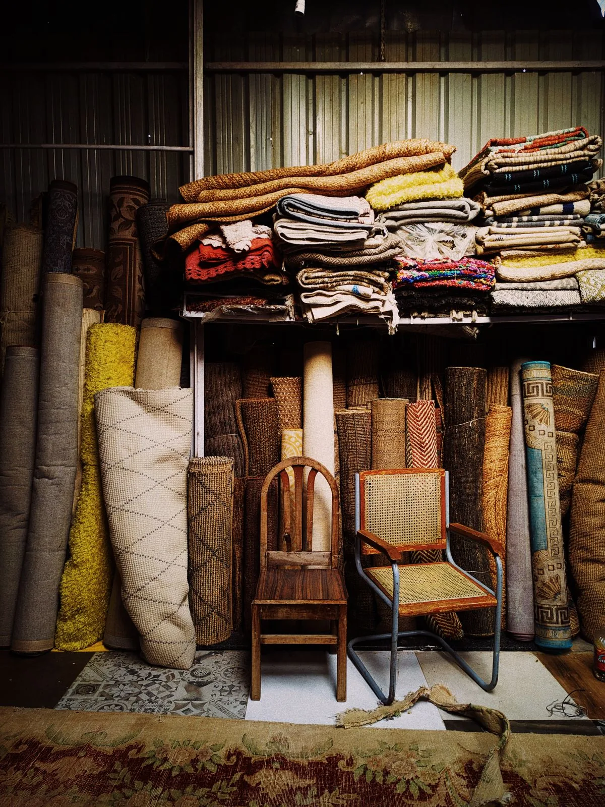 Wooden chairs and rolled and folded rugs stored inside a warehouse.