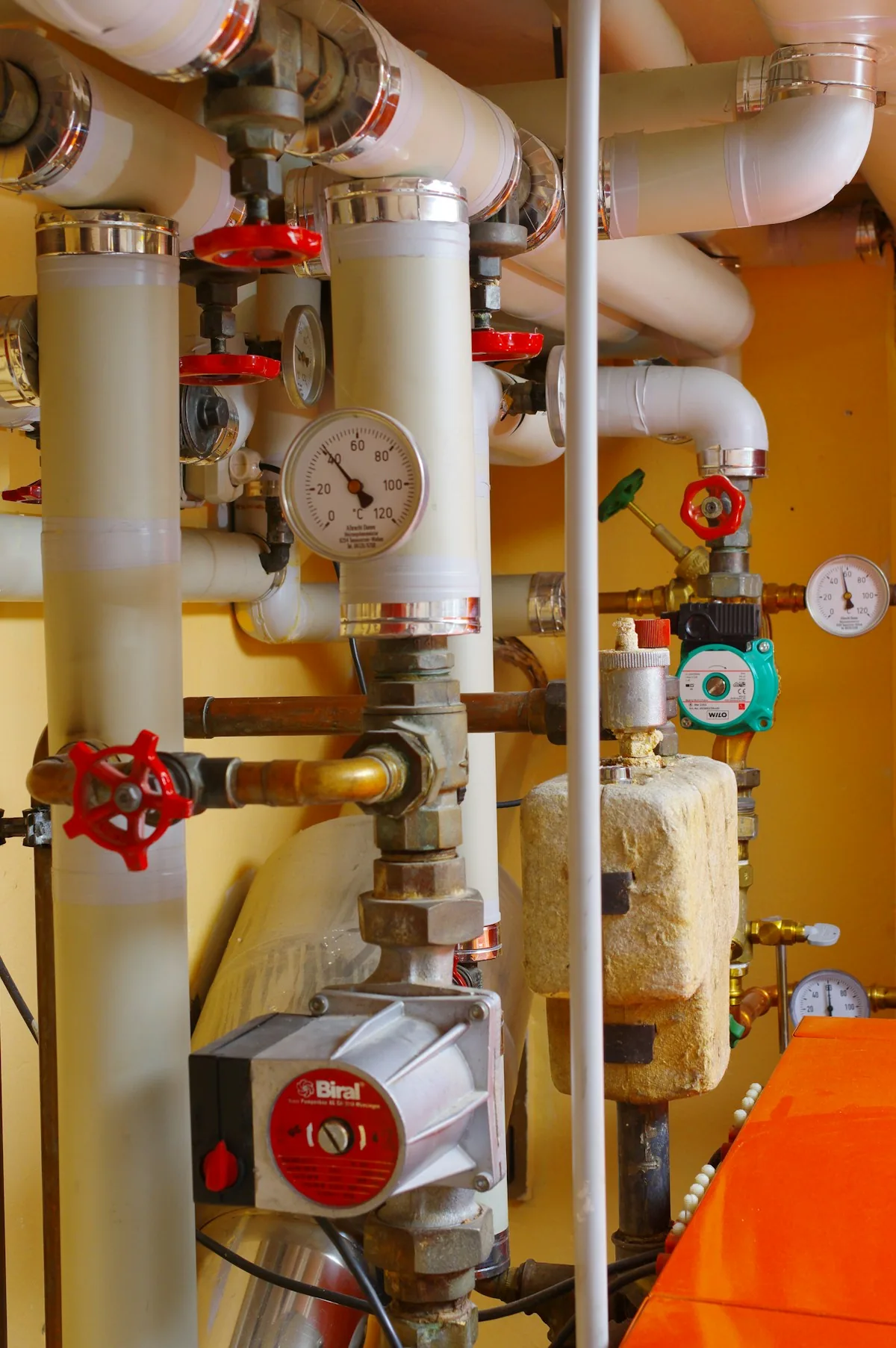 Heating-system pipework with valves, circulation pumps and round gauges.