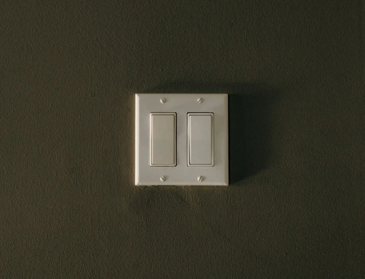 A white double rocker light switch on a dark textured wall