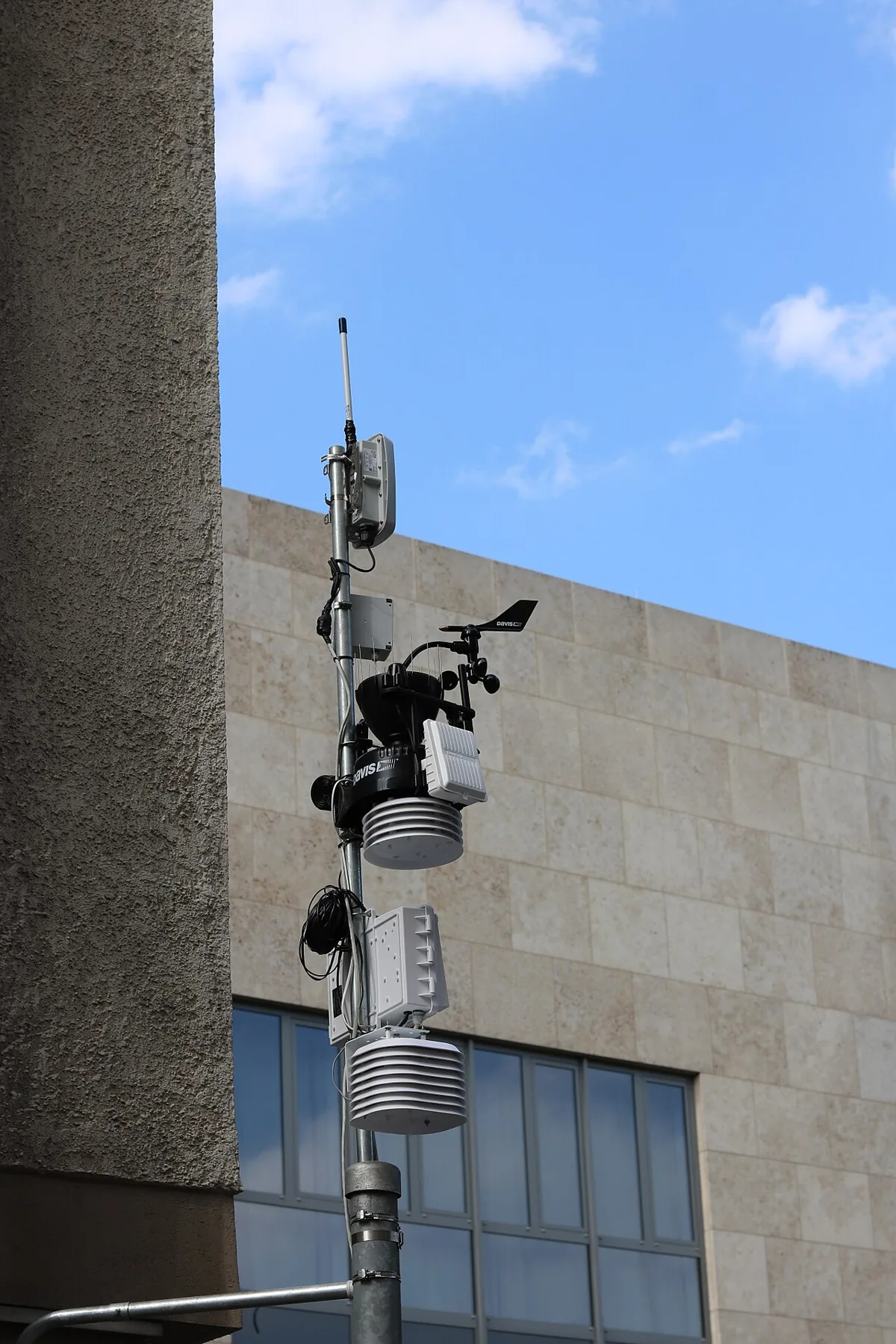Weather instruments and a small solar panel mounted on a pole beside a building.