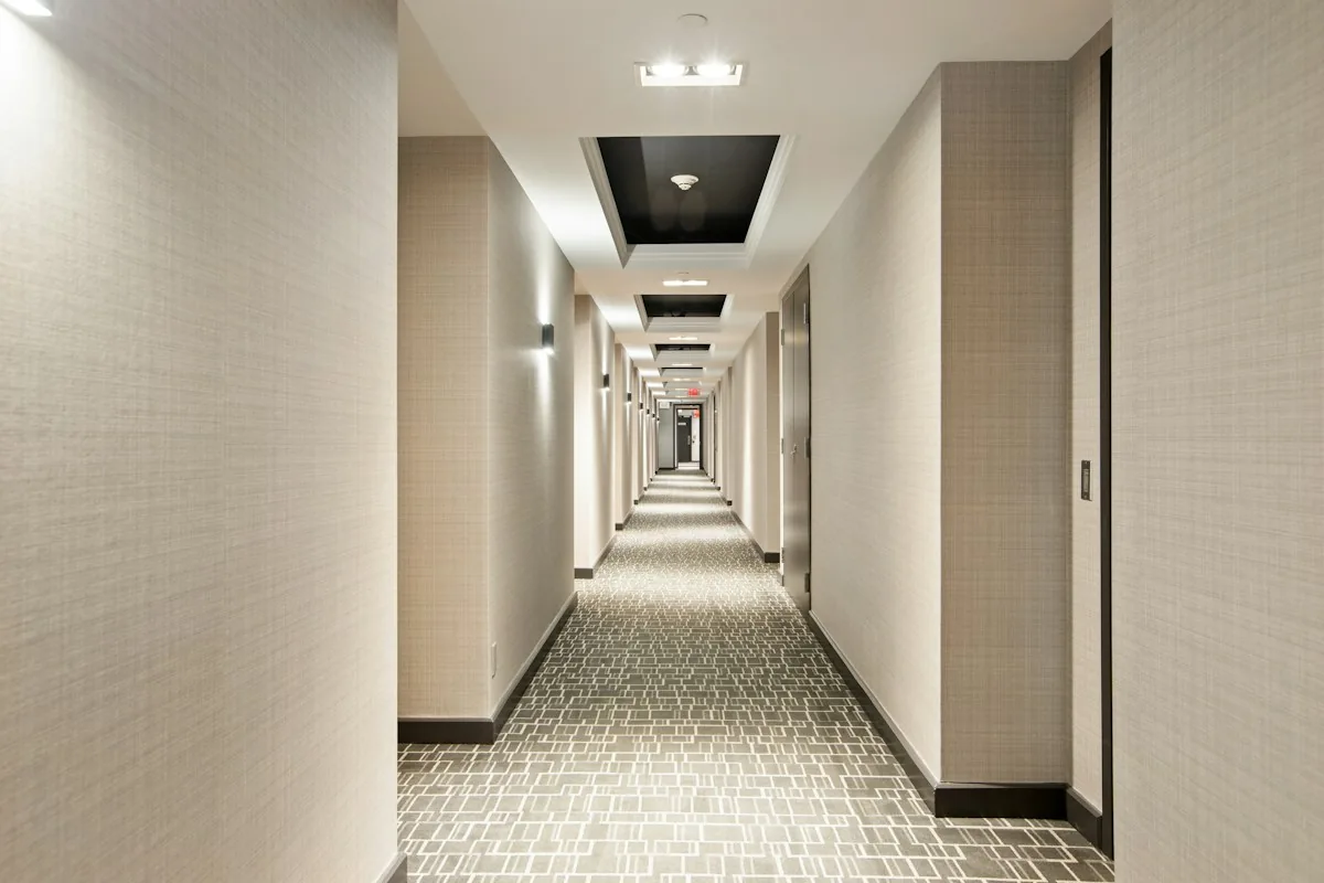 An empty hotel corridor with carpet, room doors and ceiling lights.