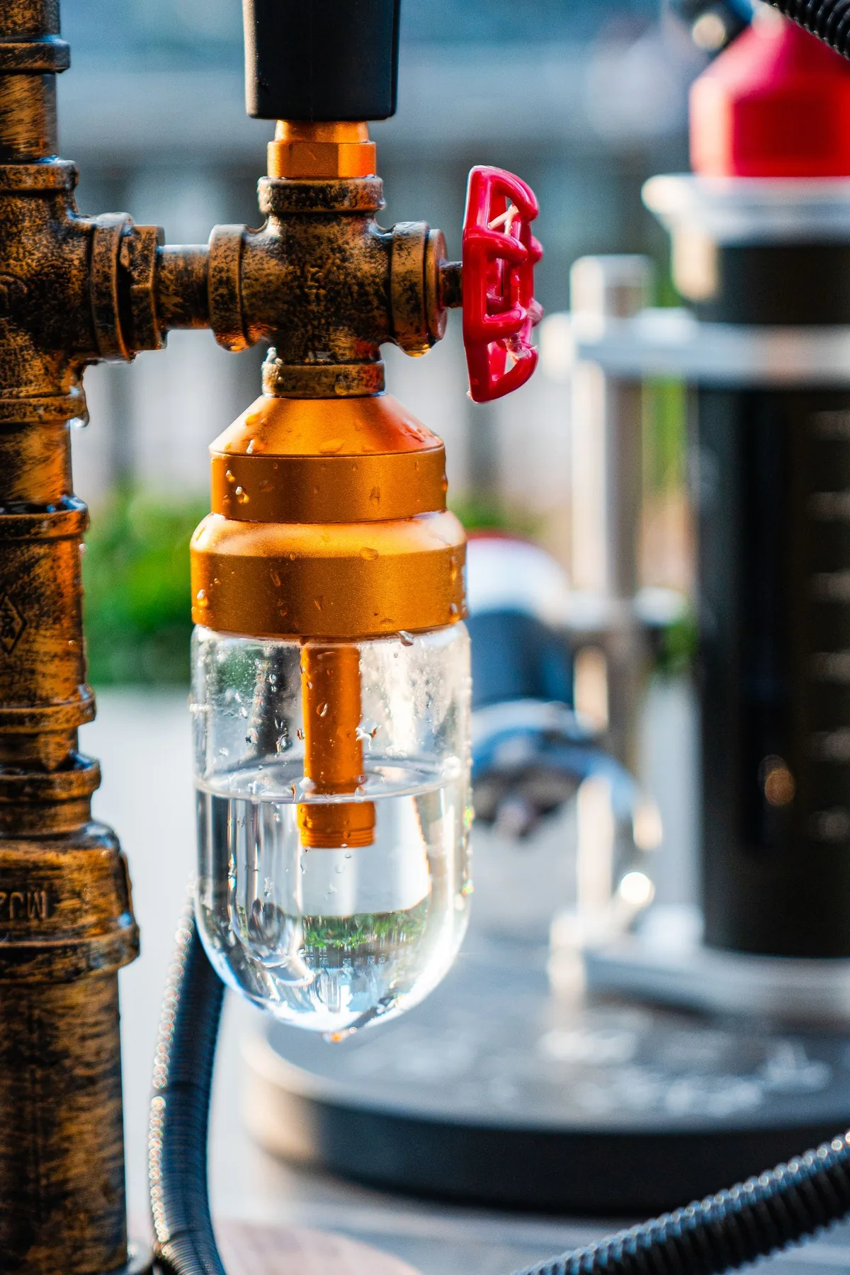 Brass valve, pipe fittings and a transparent inline filter in an industrial piping assembly.