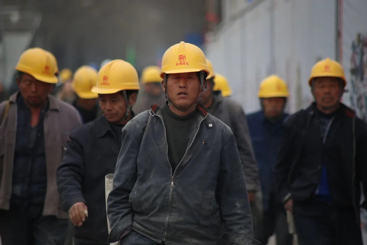 Group of workers wearing yellow hard hats walking through an outdoor industrial work area.