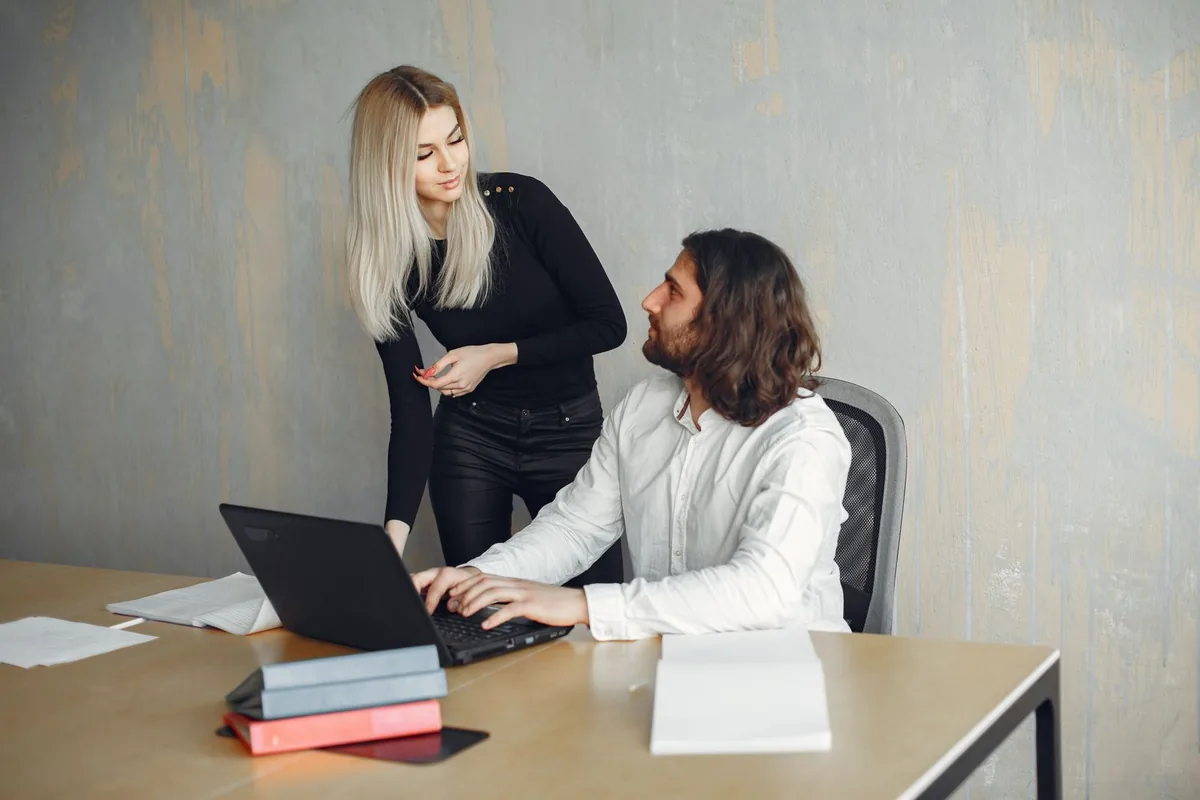Two colleagues reviewing work at a laptop with documents on the table.