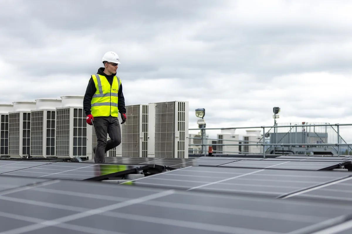Engineer wearing a hard hat and high-visibility vest beside rooftop solar panels.