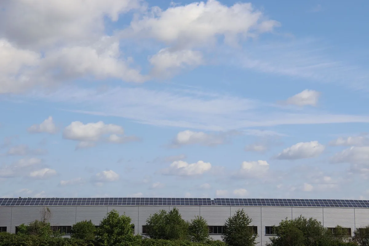 Solar panels spanning the roof of a warehouse beneath a blue sky.