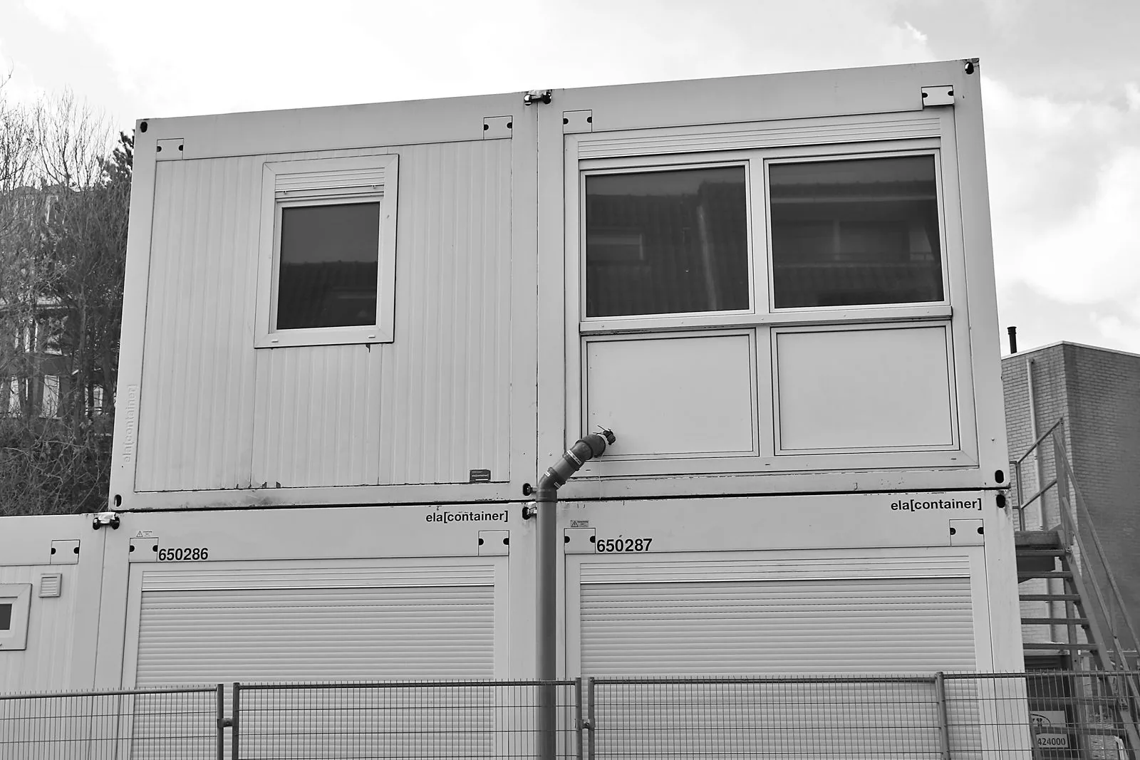 Stacked portable site-office cabins with windows and an exterior access stair.