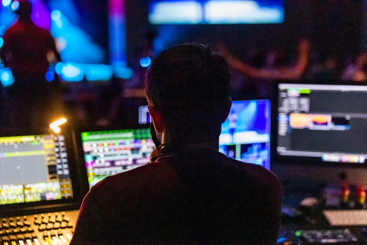 Event operator seated at a control desk with multiple monitors during a live show.