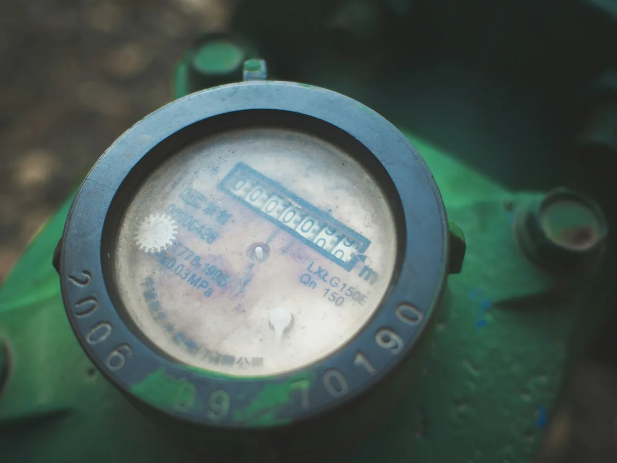 Close view of an analog water-meter register beneath a weathered glass cover.