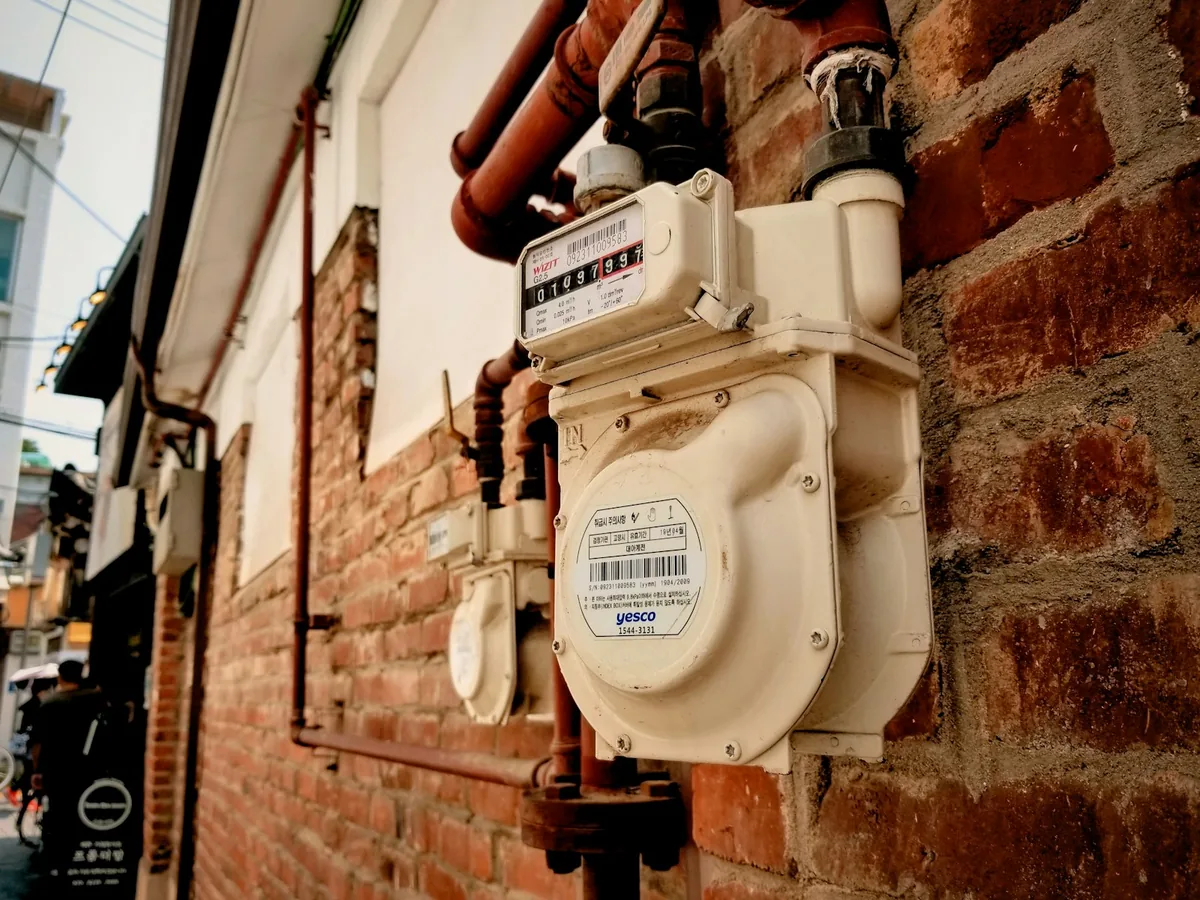 A gas meter and connected pipework mounted on a brick wall.