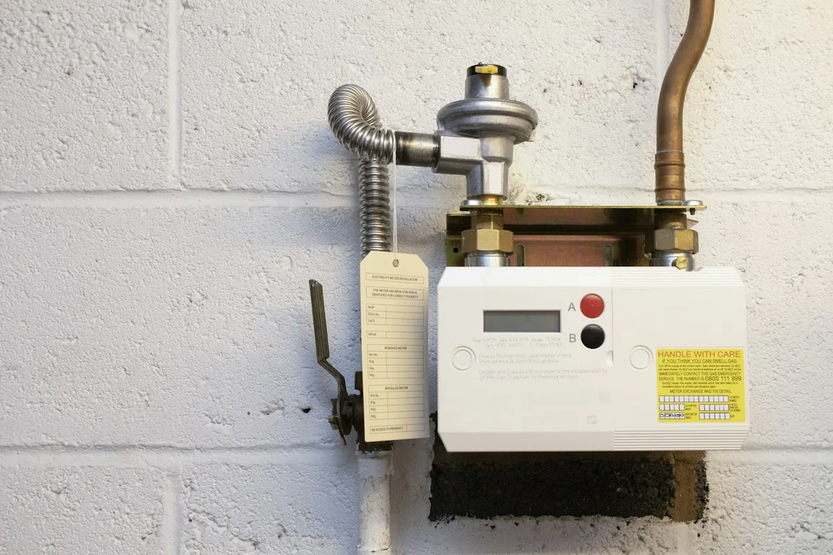 An electronic gas meter on a block wall beneath a regulator and connected pipework.