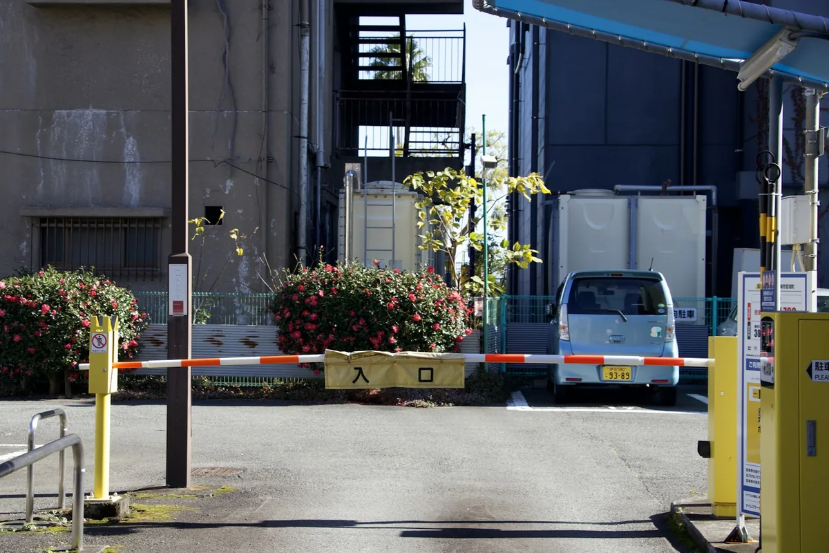 A blue van behind a lowered striped vehicle-entry barrier.