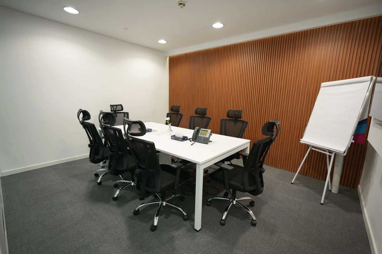 Empty office meeting room with a long white table, black chairs, and a flip chart.