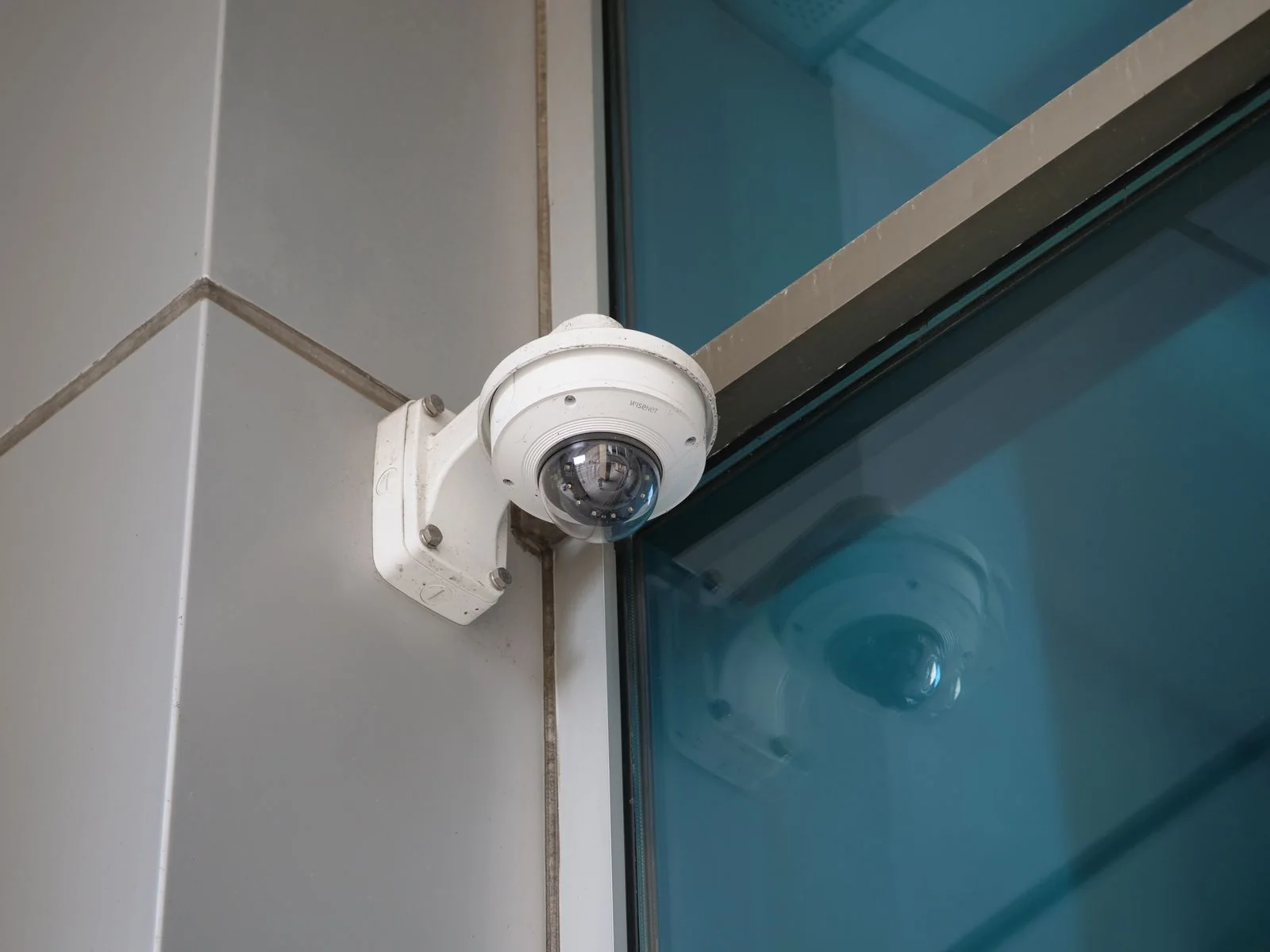 White dome security camera mounted beside blue glass on a building corner.