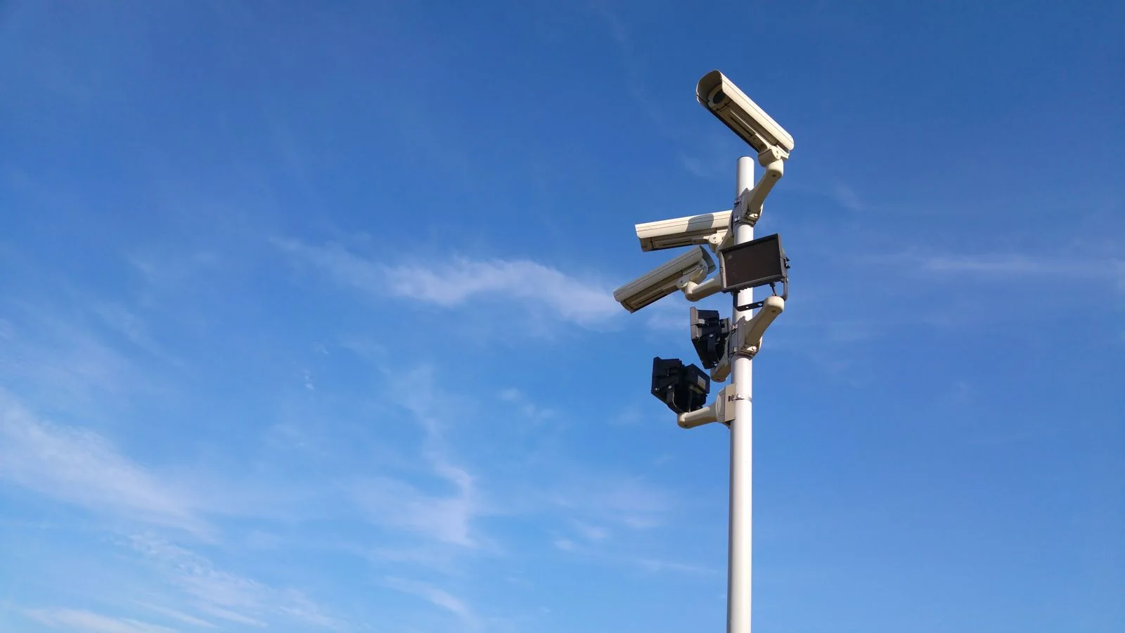 Several surveillance cameras mounted at different angles on a pole beneath a blue sky.