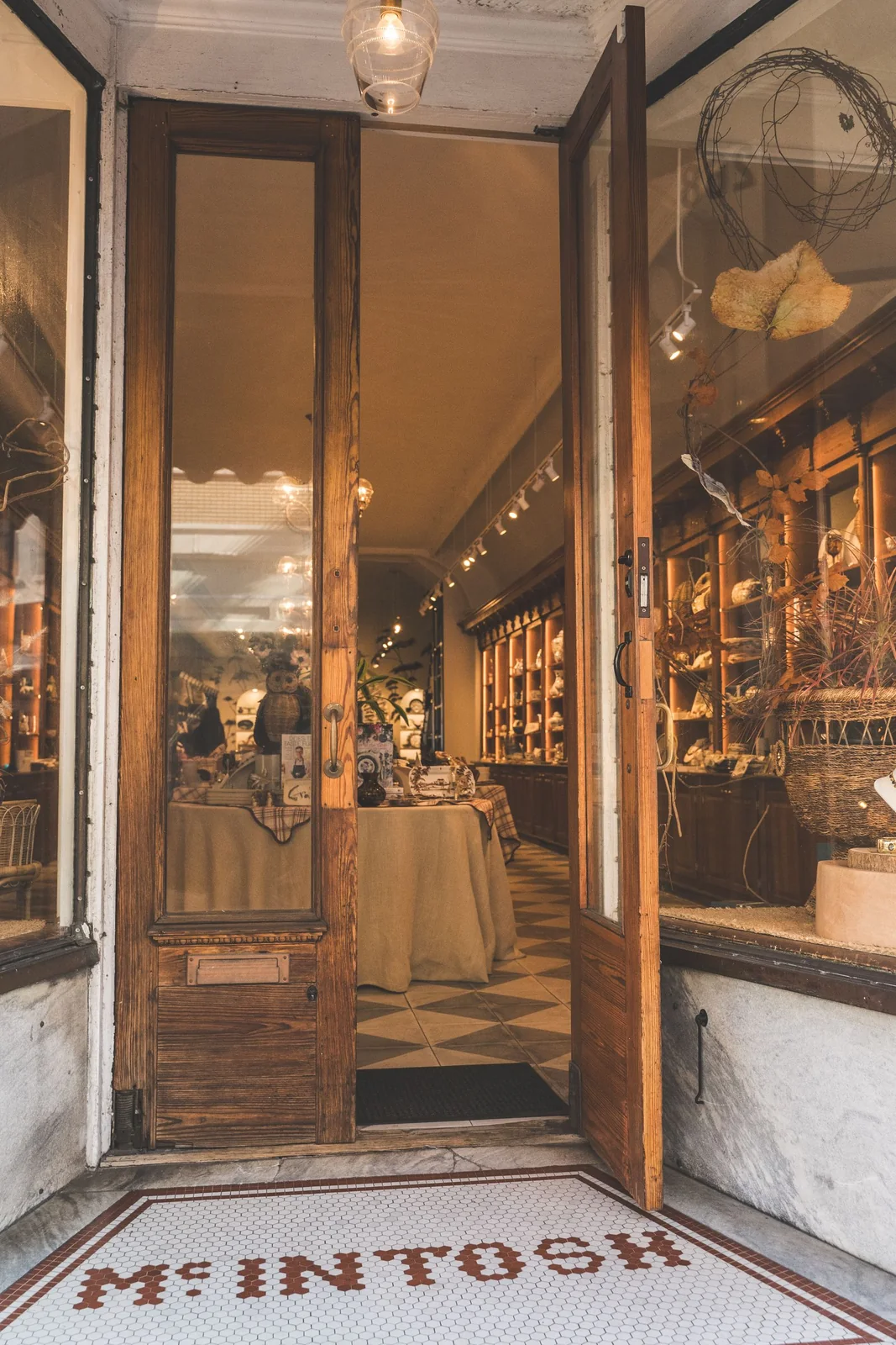 Open wooden and glass door leading into a warmly lit shop with display shelves.