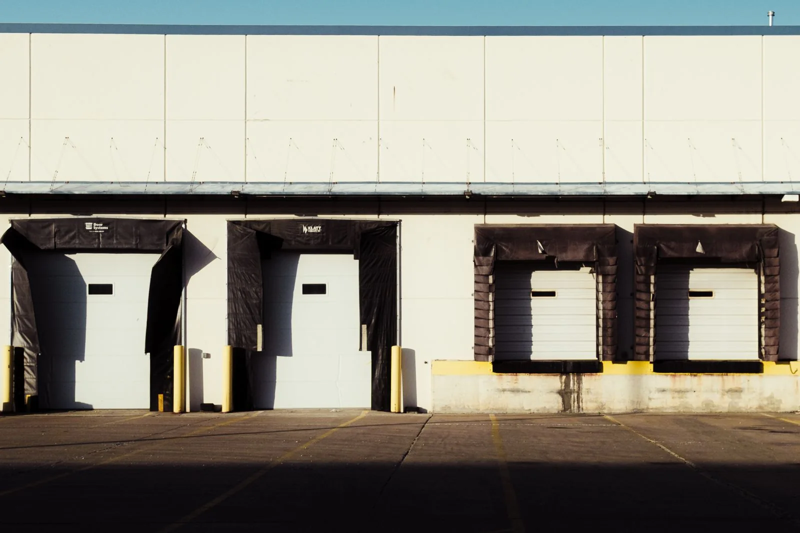 Closed loading-bay doors and dock shelters along a sunlit industrial building.