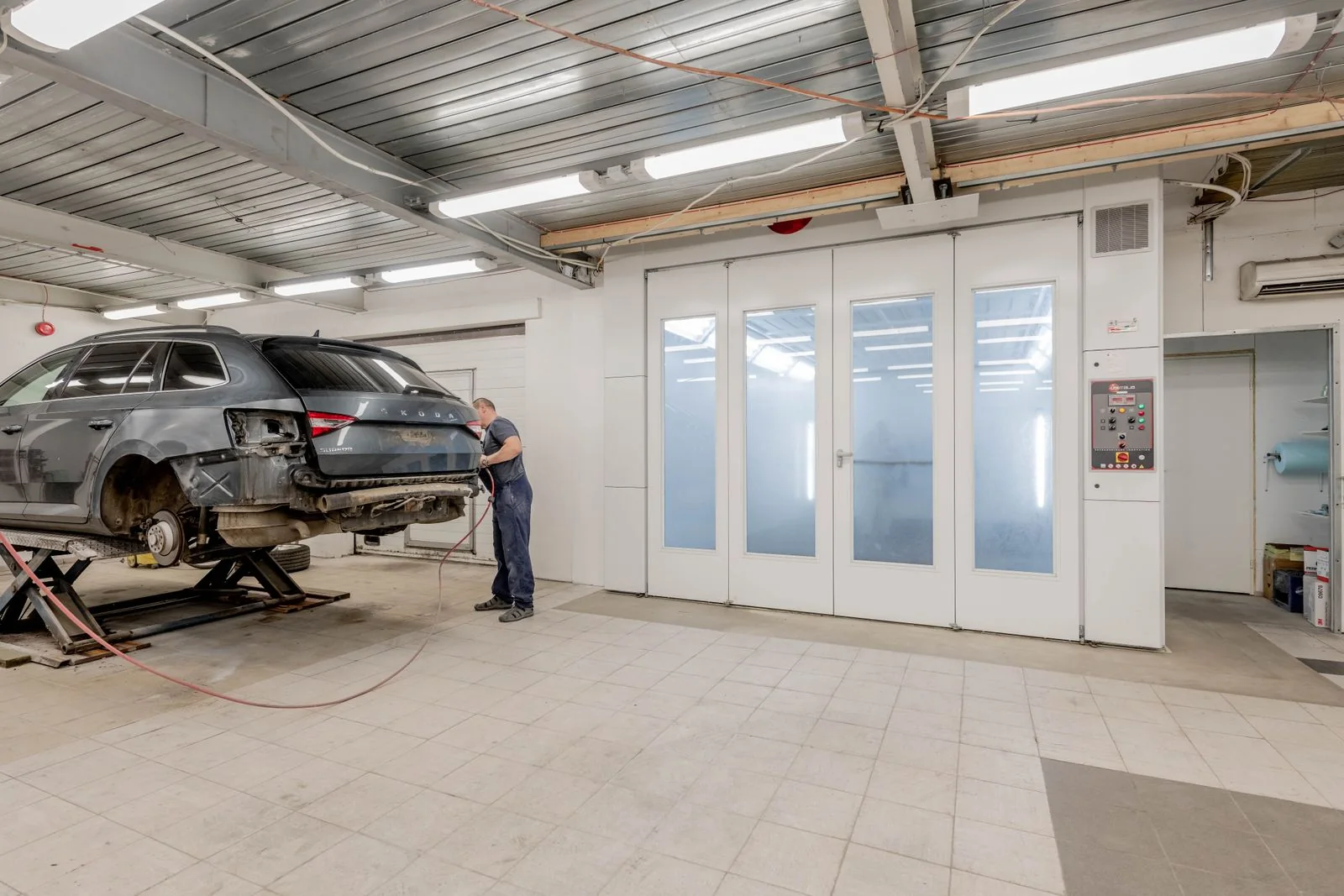Car raised inside a bright automotive workshop beside a bank of tall white doors.