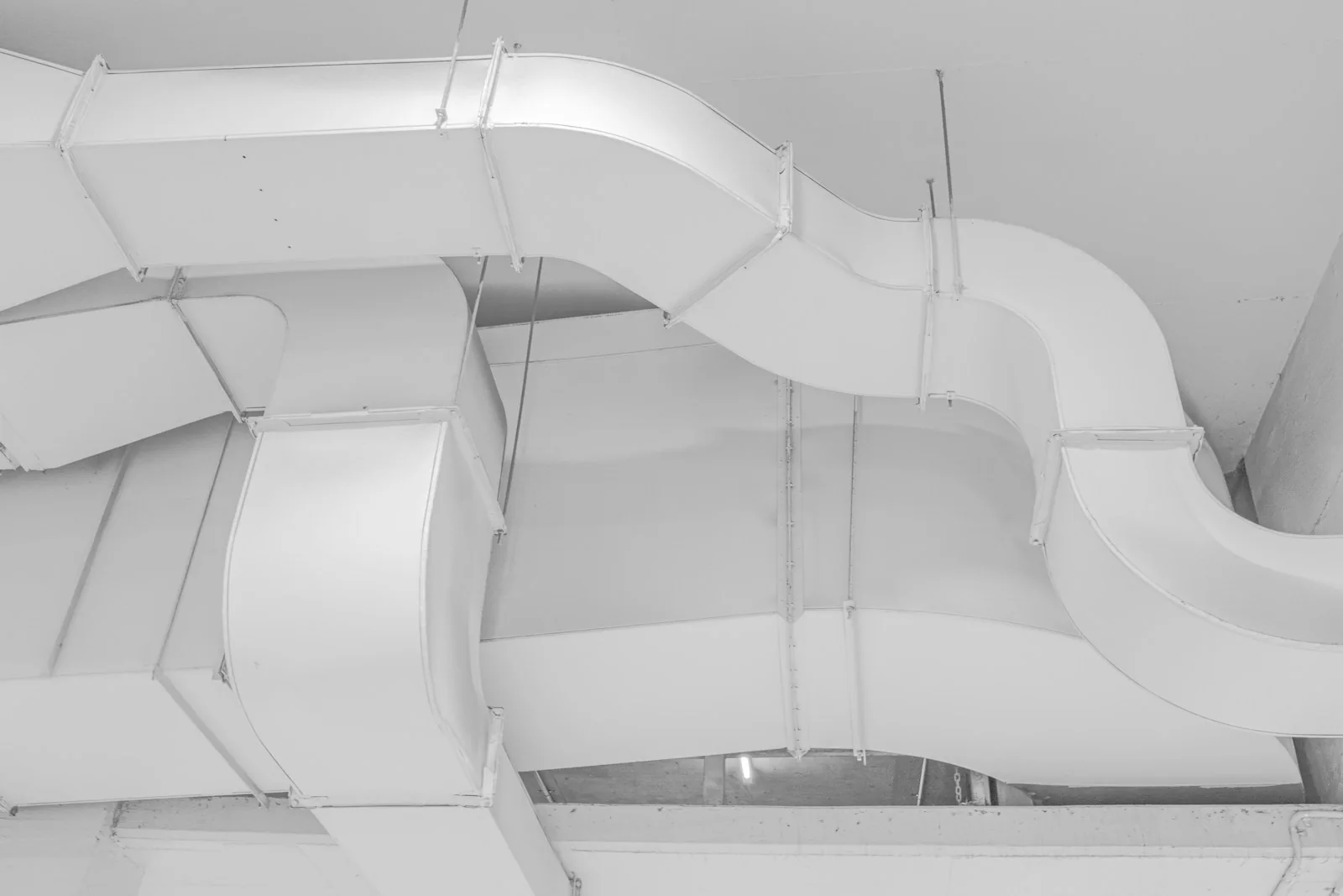 White ventilation ducts suspended beneath a concrete ceiling.