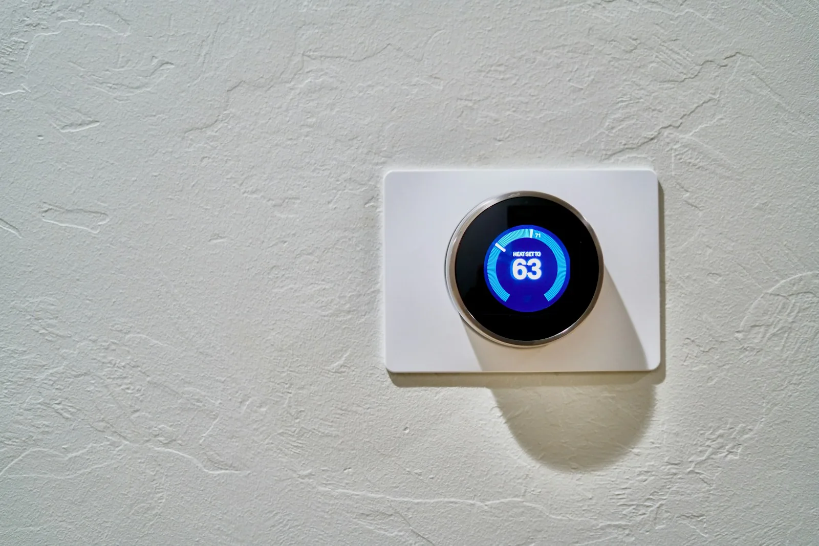 A wall-mounted round thermostat with an illuminated temperature setting.