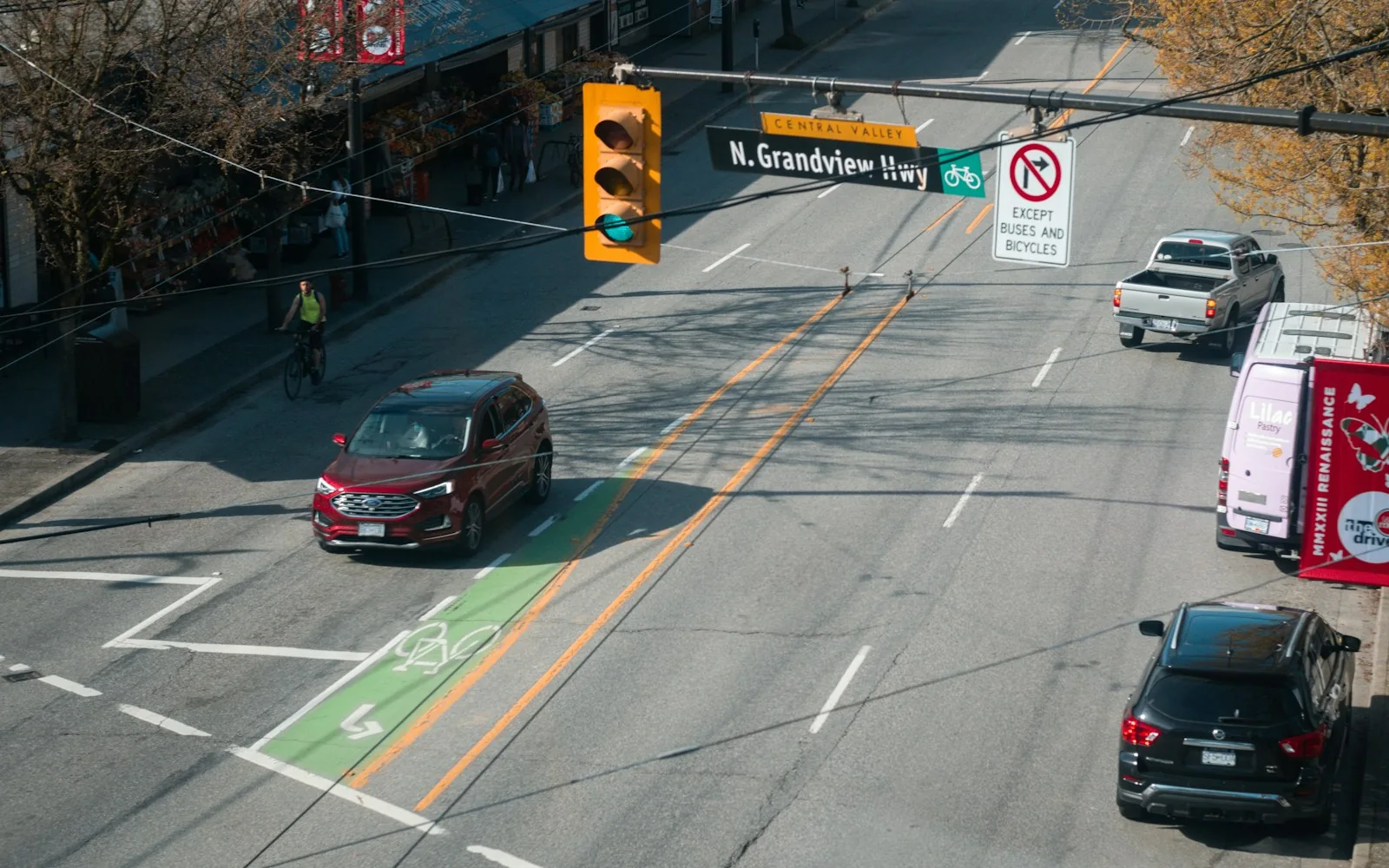 Cars approaching traffic signals beside marked bicycle lanes on a city street.