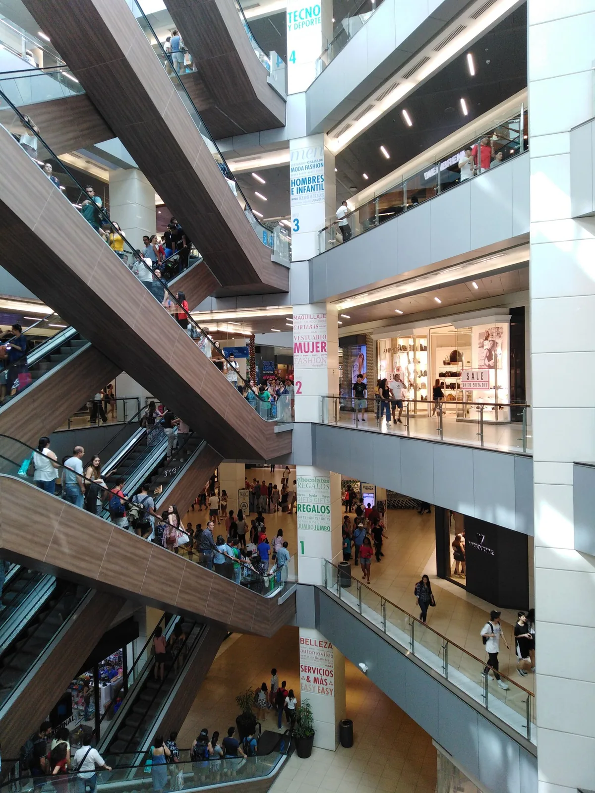 Shoppers moving between floors and escalators in a multilevel shopping mall.