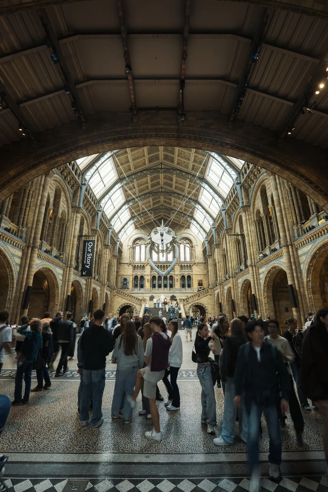 Visitors walking through a tall museum atrium beneath a vaulted roof and suspended whale skeleton.