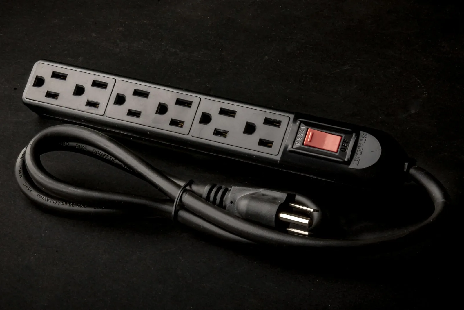 An unplugged black power strip with six US-style grounded outlets, a red switch and a coiled power cord.