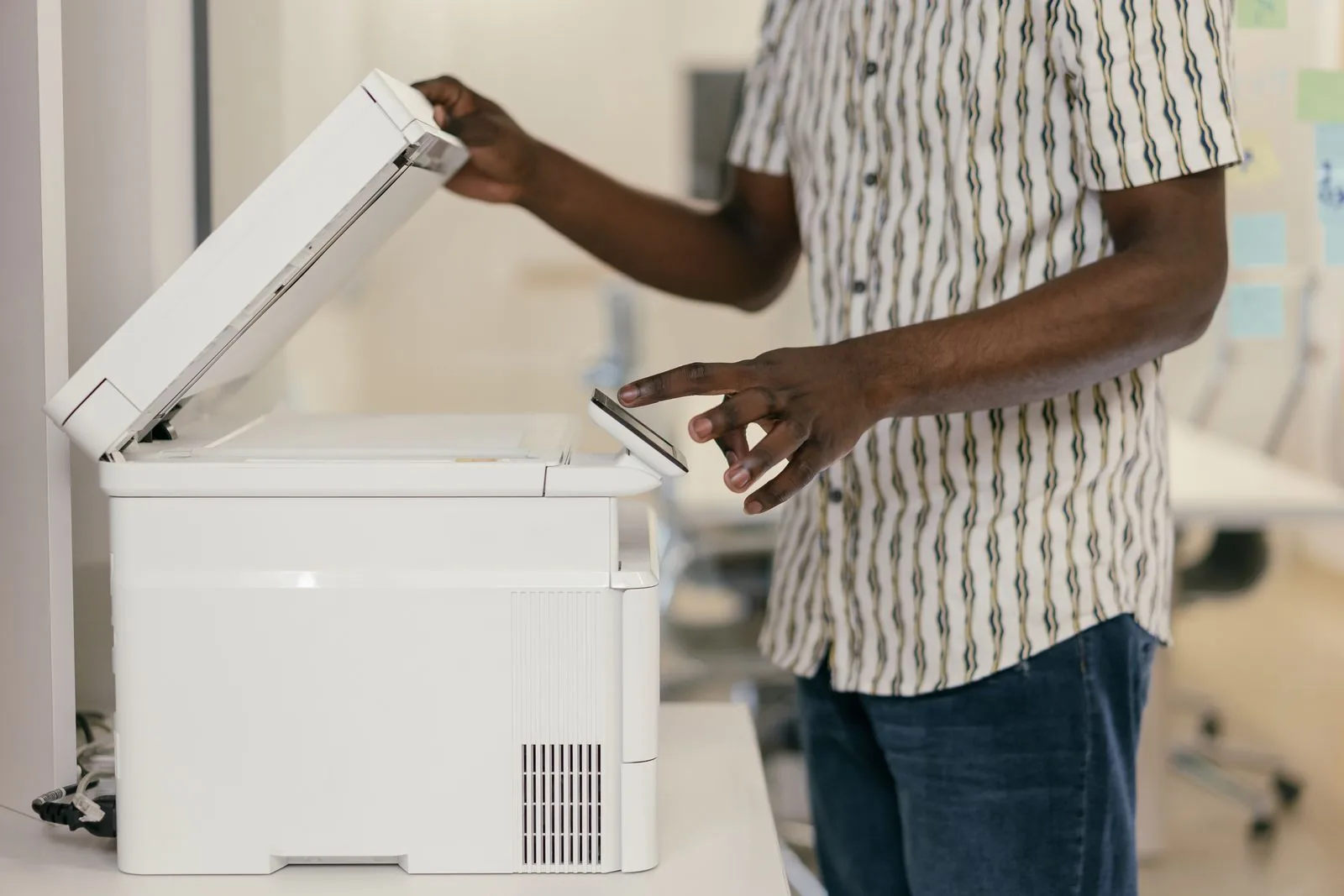A person operating a white multifunction office printer with its scanner lid open.