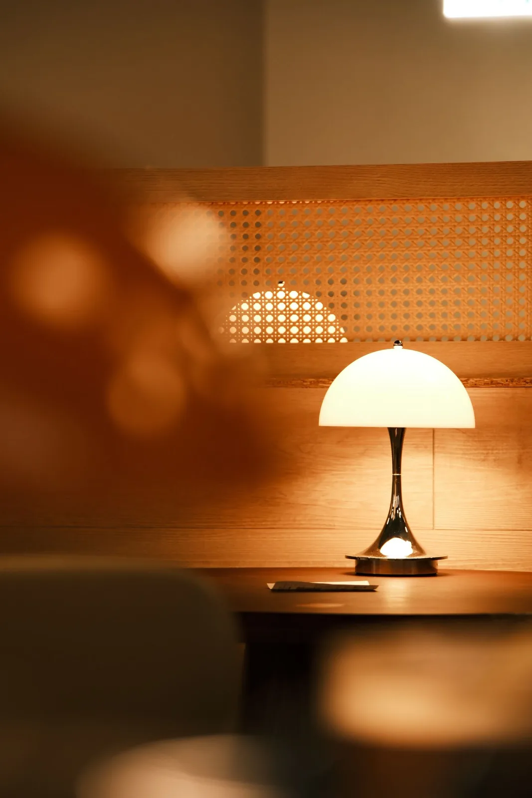 An illuminated table lamp on a wooden surface in a warmly lit interior.