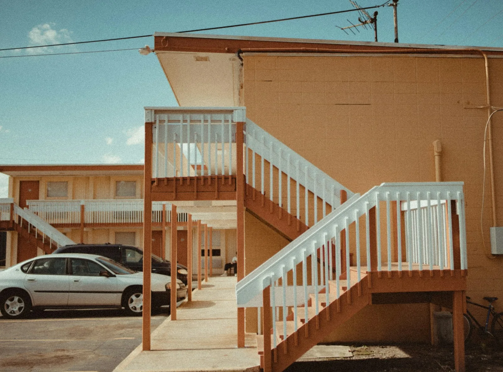 Exterior stairs, balconies and a parked car outside a two-story motel.