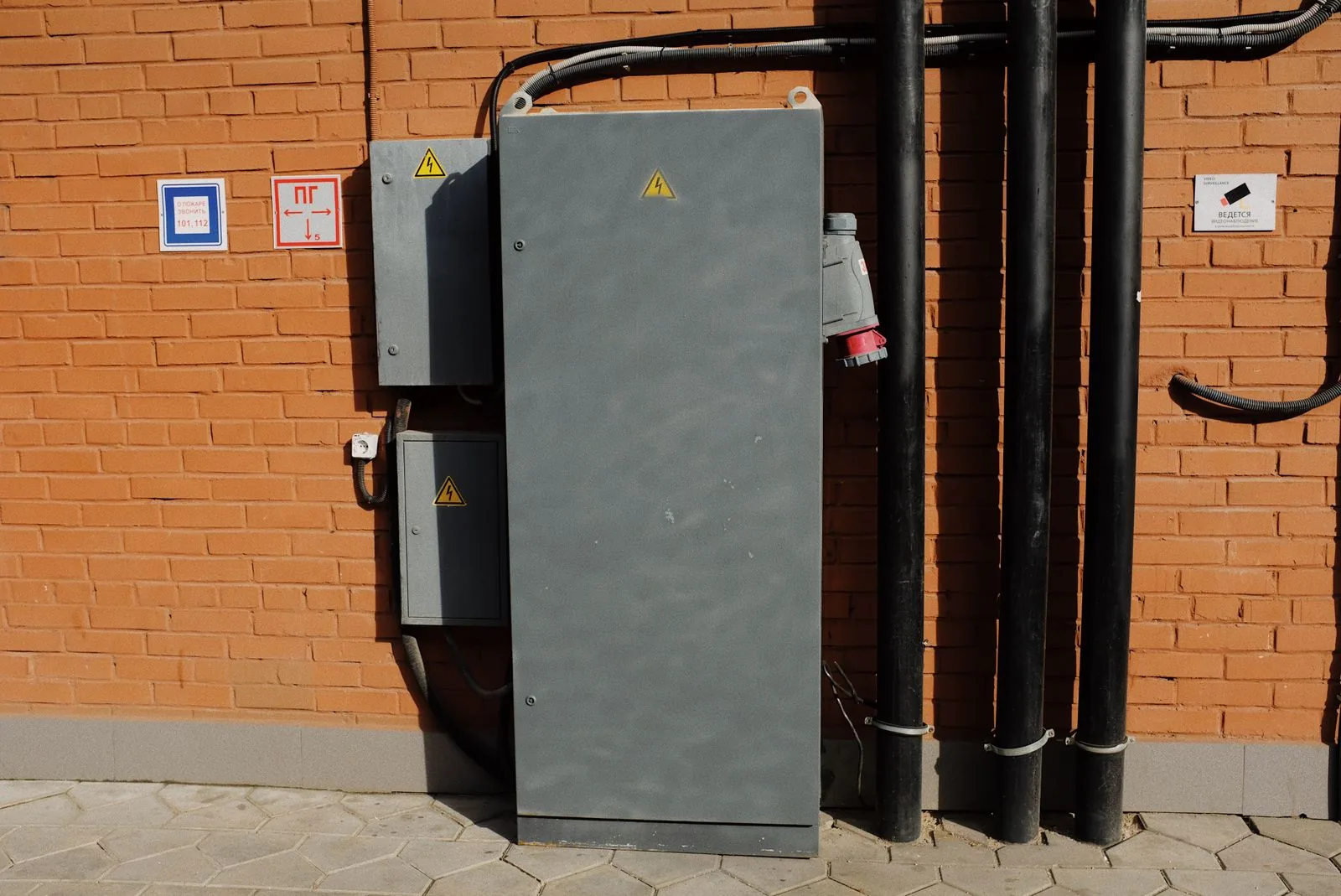 Gray electrical service cabinets and black conduit against a brick wall.