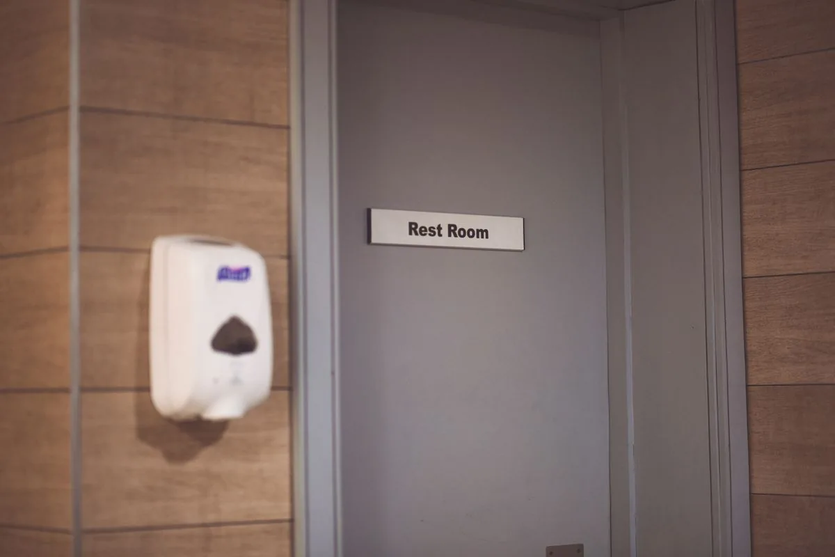 A closed door marked Rest Room beside a wall-mounted dispenser.