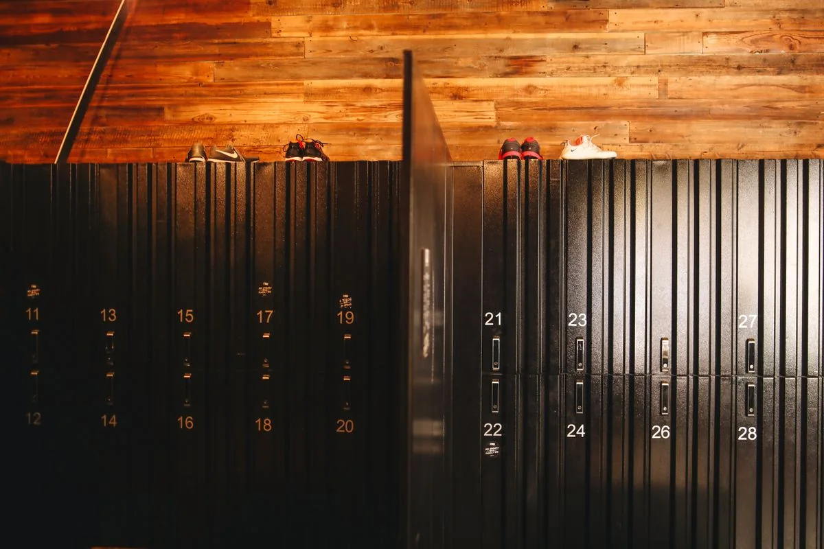 Black numbered lockers beneath a wooden wall with shoes resting on top.