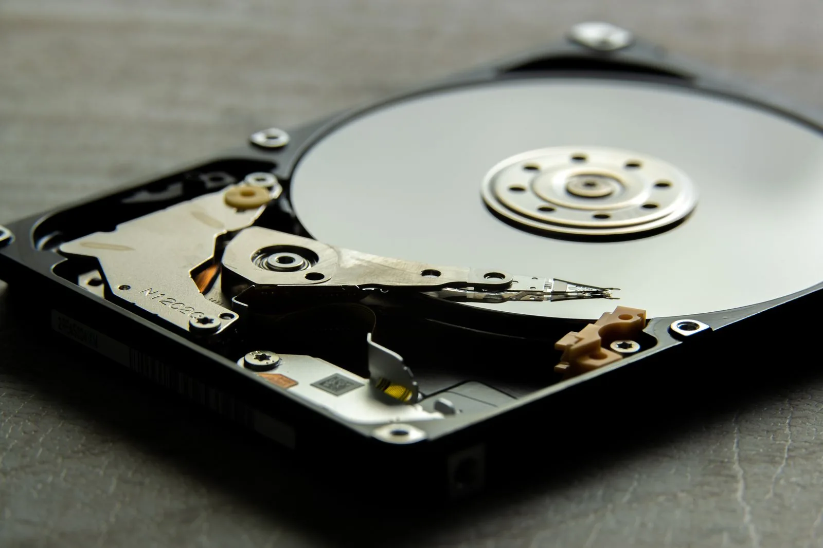 Exposed hard-drive platter and actuator arm on a gray work surface.