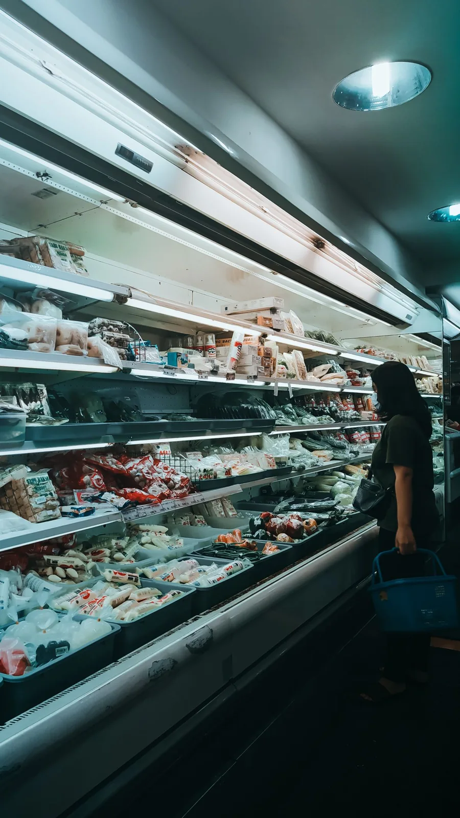 A shopper beside refrigerated food shelves in a supermarket aisle.