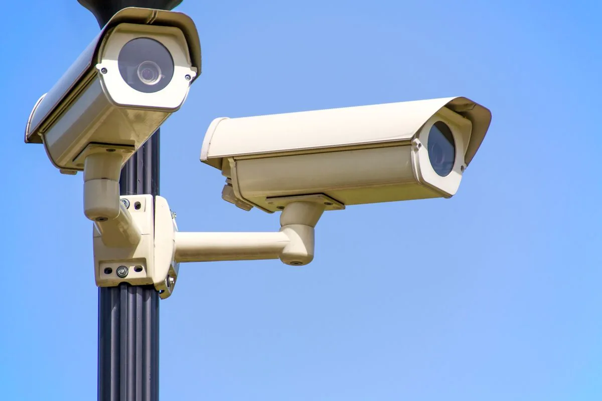 Two outdoor surveillance cameras on a pole against a clear blue sky.