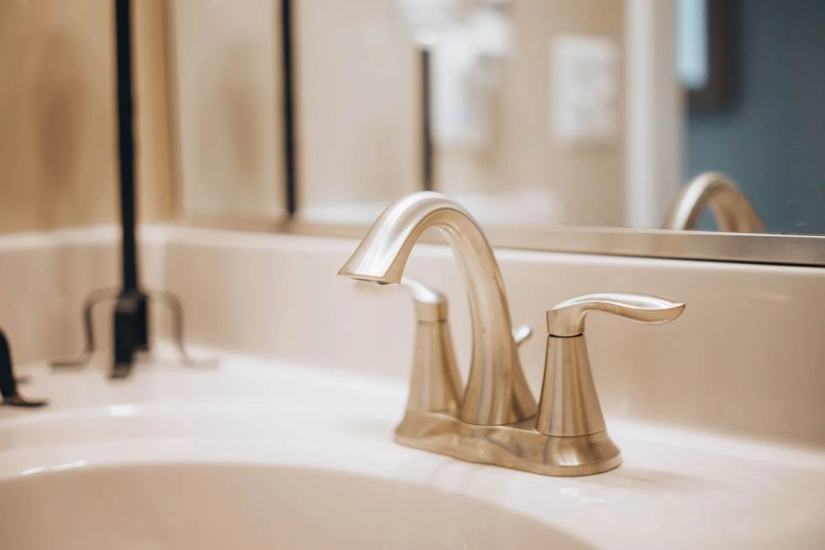 Brushed metal faucet above a white bathroom sink with a mirror behind it.