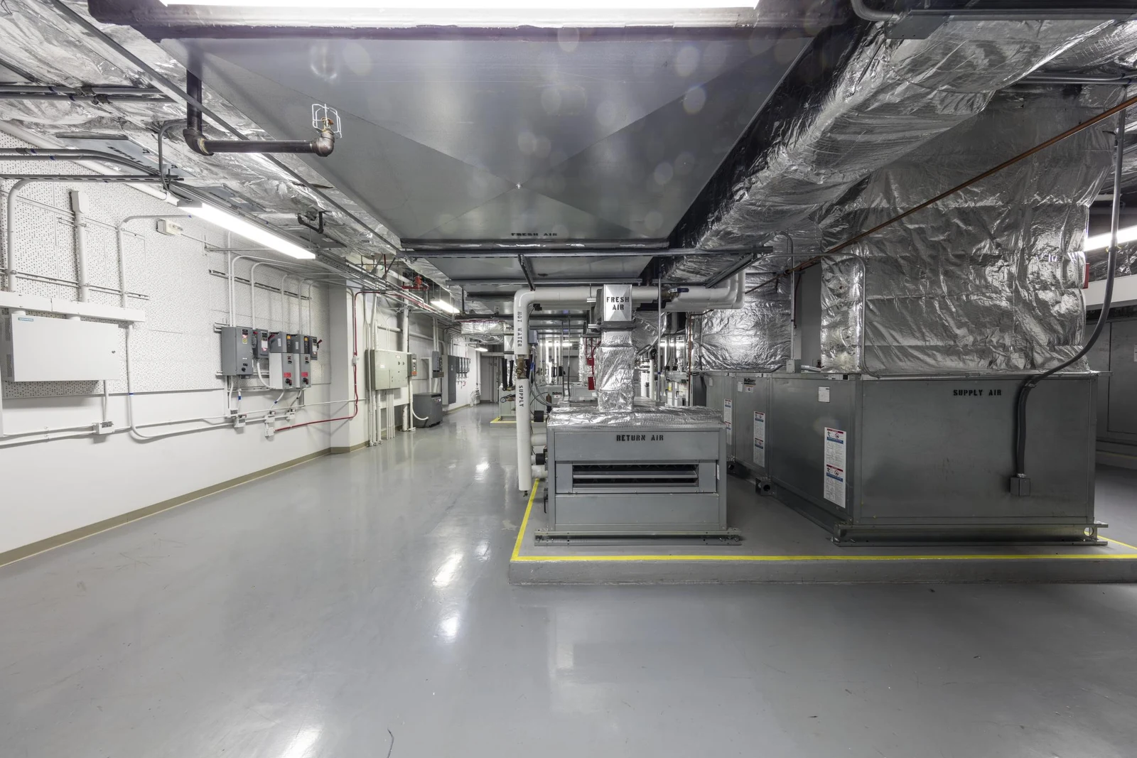 Air-handling units, insulated ventilation ducts and wall-mounted controls in a Los Angeles building mechanical room.